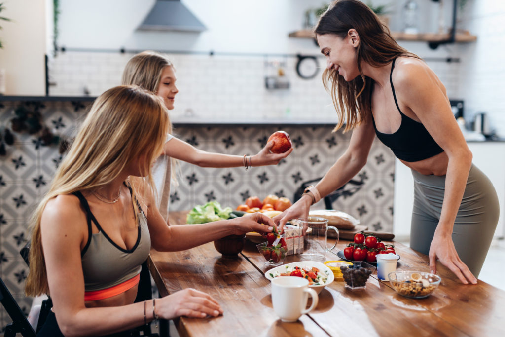 Athletic woman prepares a snack for her friend and daughter after a light workout at home.